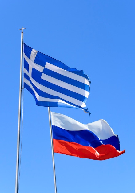 Le bandiere della Grecia e della Russia volano nel vento contro il cielo blu