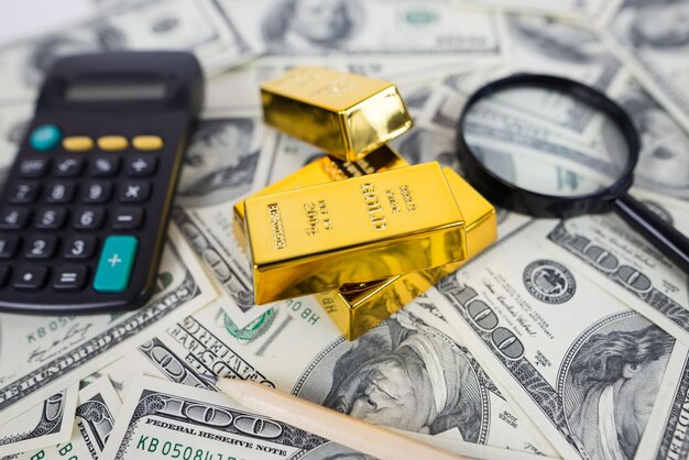 le barre d'oro si trovano con una calcolatrice e una lente d'ingrandimento accanto a una grande quantità di dollari concetto di risparmio finanziario oro e dollari