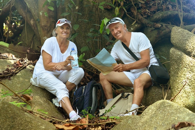 Le belle coppie anziane felici riposano al resort tropicale con zaini e mappa