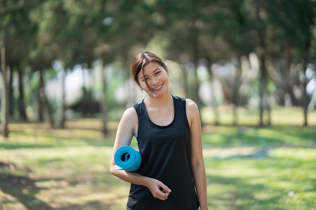 Le belle donne che tengono la stuoia di yoga si preparano ad esercitare lo yoga in giardino