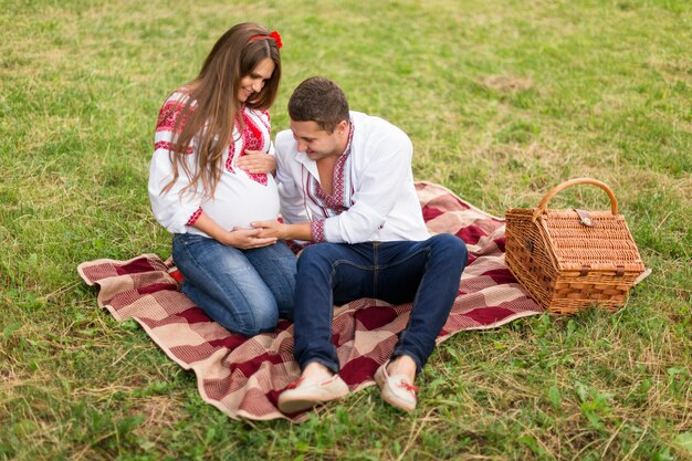 Le belle giovani coppie incinte si sono vestite nello stile ucraino nazionale che ha picnic nel parco di autunno. Concetto di felicità maternità e famiglia.