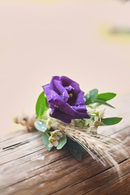 Le bugie porpora di boutonniere dello sposo delicato su un fondo leggero di legno