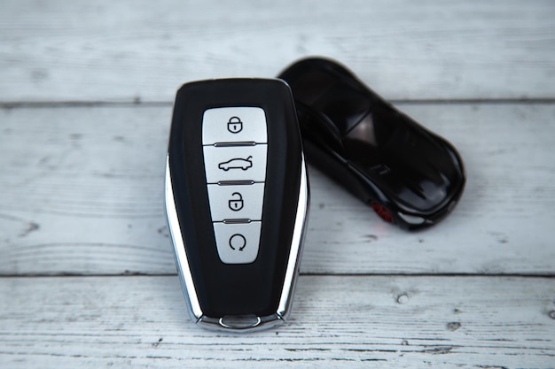 Le chiavi della macchina sono nere con inserti metallici e pulsanti automatici su uno sfondo di legno bianco
