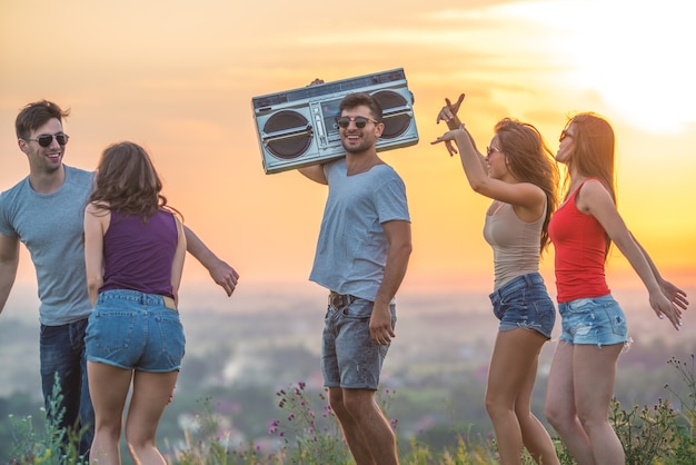 Le cinque persone che ballano con un boom box sullo sfondo del tramonto