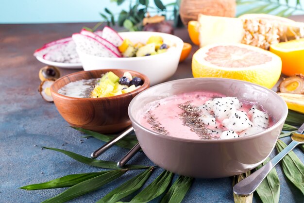 Le ciotole rosse o rosa di acai del frullato hanno superato con i semi freschi di chia e di pitaya su foglia di palma su fondo di pietra, spazio della copia