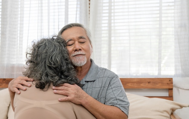 Le coppie anziane asiatiche pensionate felici si abbracciano mentre sono sedute sul divano nel soggiorno di casa con amore e cura.