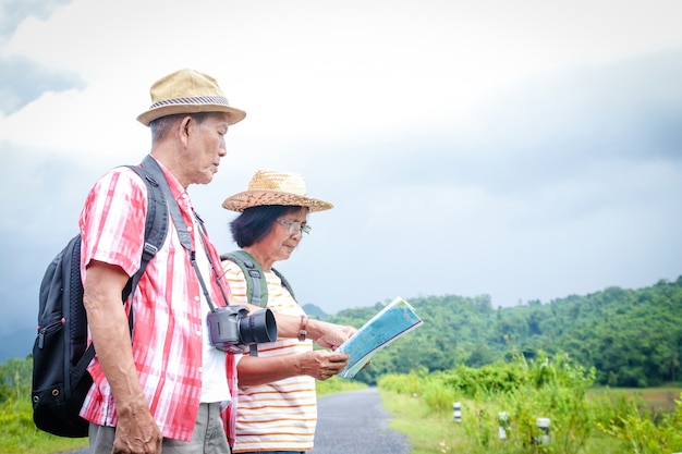 Le coppie asiatiche anziane viaggiano nella foresta, portando una mappa per studiare il percorso.