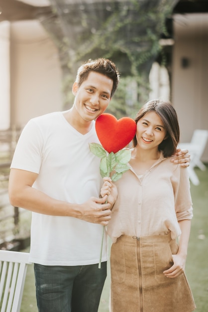 Le coppie asiatiche in amore che tengono il cuore modellano il fiore. Concetto di giorno vanlentine.