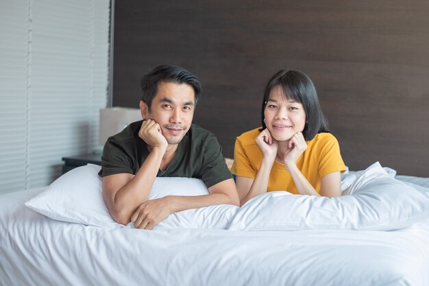 Le coppie asiatiche sorridono e guardando la fotocamera sul letto bianco a casa