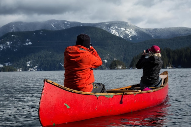 Le coppie di amici su una canoa di legno stanno pagaiando in un'insenatura circondata dalle montagne canadesi