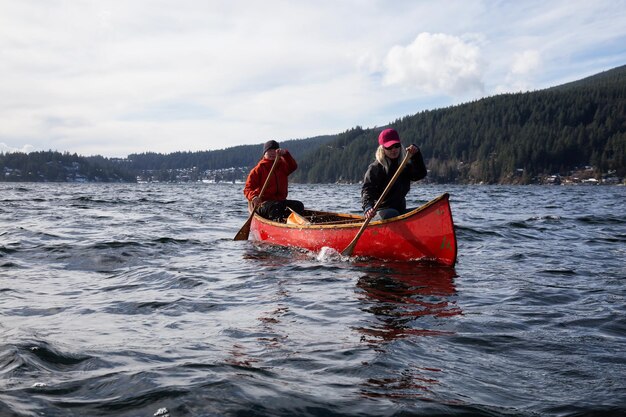 Le coppie di amici su una canoa di legno stanno pagaiando in un'insenatura circondata dalle montagne canadesi