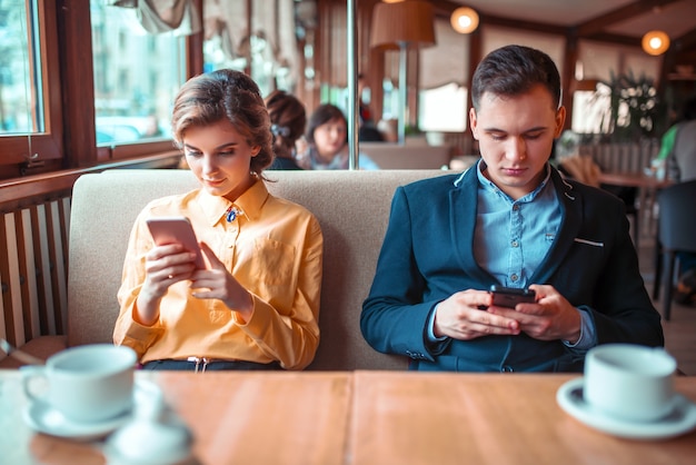 Le coppie di amore usano i loro telefoni cellulari nel ristorante.