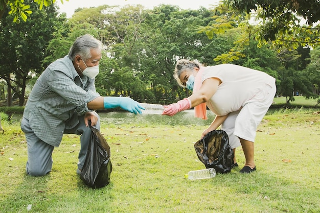 Le coppie di anziani che indossano maschere mettono bottiglie di plastica in sacchetti neri per mantenere pulito il giardino