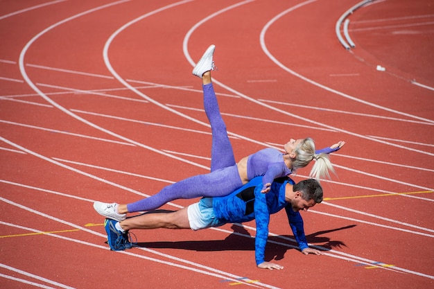 Le coppie di fitness sportive che si allenano insieme stanno in piedi sulla tavola e fanno push up sulla pista dello stadio all'aperto indossando abbigliamento sportivo, sport e fitness.