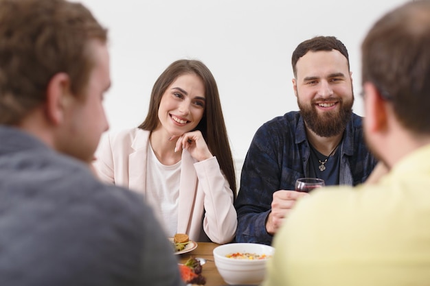 Le coppie felici cenano con gli amici, festa a casa. Le persone mangiano insieme, conversazione amichevole