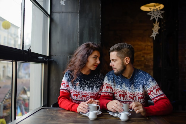 Le coppie felici e romantiche in maglioni caldi bevono il caffè dalle tazze di carta a gettare in caffetteria.