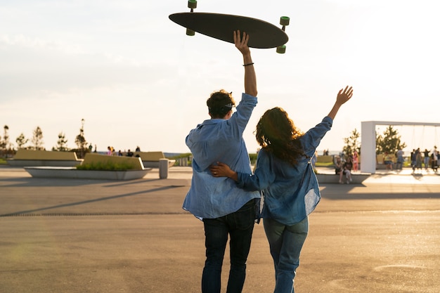 Le coppie felici godono dell'abbraccio del tramonto con le braccia alzate tengono il concetto di felicità e libertà del longboard