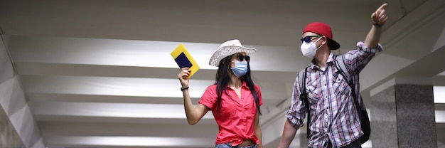 Le coppie felici nella mascherina medica protettiva vanno tunnel sul terminale di arport e tengono il passaporto in ritratto della mano. Viaggia dopo il concetto di covid 19