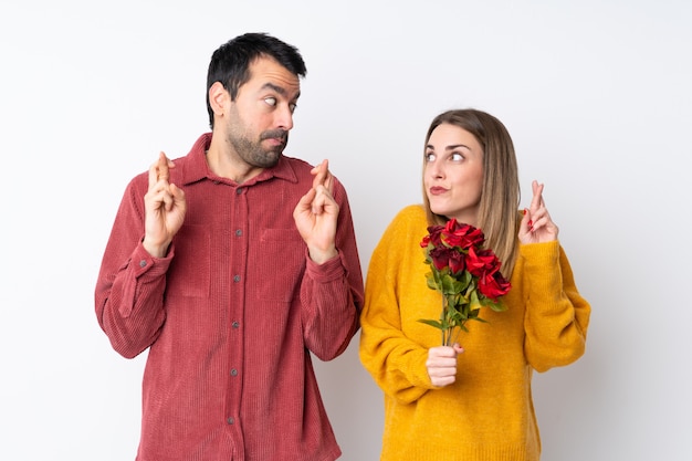 Le coppie in Valentine Day che tengono i fiori sopra la parete isolata con le dita che attraversano e che desiderano il meglio