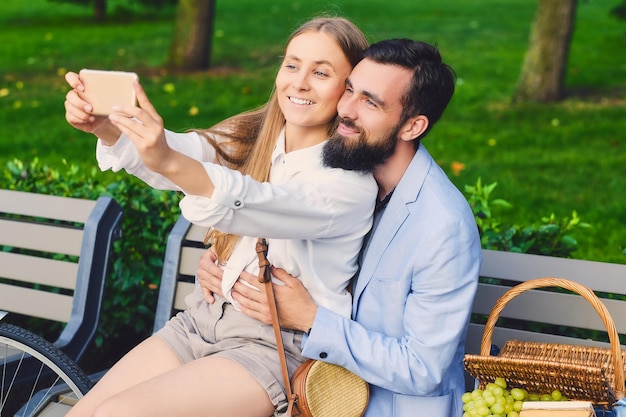 Le coppie moderne felici ad un appuntamento fanno selfie in un parco.