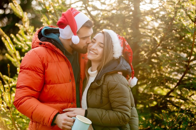 Le coppie romantiche in cappelli di Natale si avvicinano all'albero di abete.