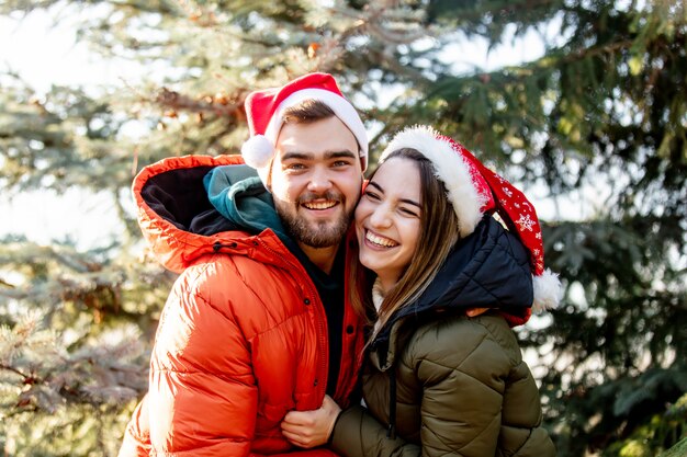 Le coppie romantiche in cappelli di Natale si avvicinano all'albero di abete.