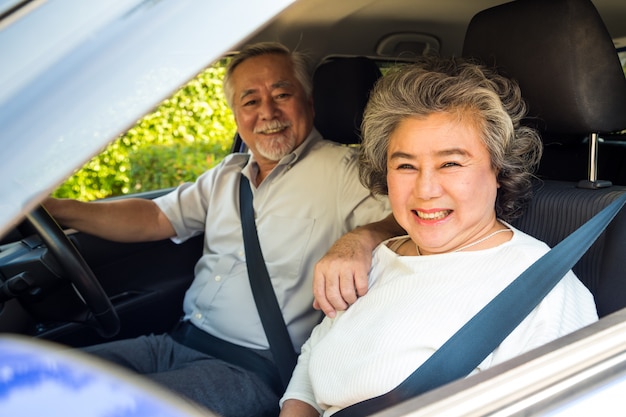 Le coppie senior asiatiche che guidano un'automobile e sorridono felicemente con l'espressione positiva felice durante l'azionamento per viaggiare viaggio, la gente gode di di ridere il trasporto sul concetto di viaggio stradale