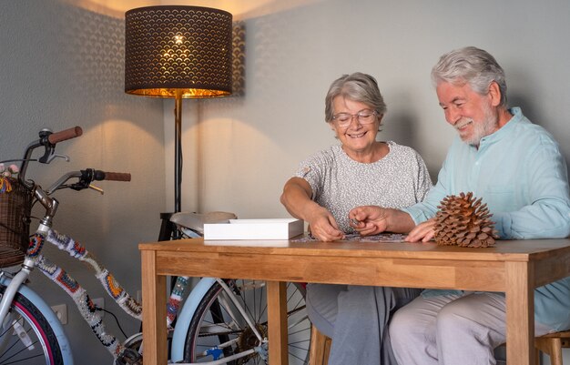 Le coppie senior felici a casa trascorrono del tempo insieme facendo un puzzle sul tavolo di legno.