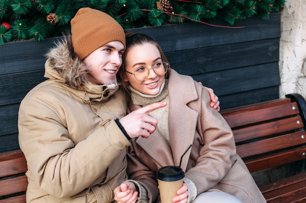 Le coppie turistiche si divertono insieme in inverno sulla strada seduti sulla panchina, bevendo caffè