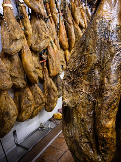 Le cosce di maiale essiccate sono appese al mercato della carne. Piatto nazionale spagnolo di prosciutto o jamon in una drogheria. Acquisto di maiale iberico nel supermercato Spagna. Prosciutto secco e stagionato appeso. Il mercato vende prodotti a base di carne cruda