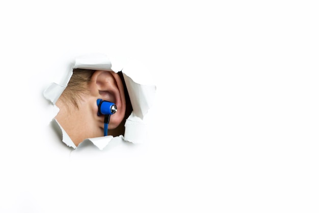 Le cuffie blu nell'orecchio sporgono da un foro su uno sfondo bianco