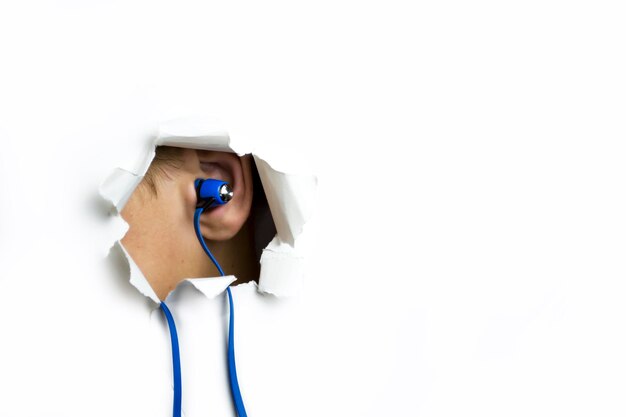 Le cuffie blu nell'orecchio sporgono da un foro su uno sfondo bianco
