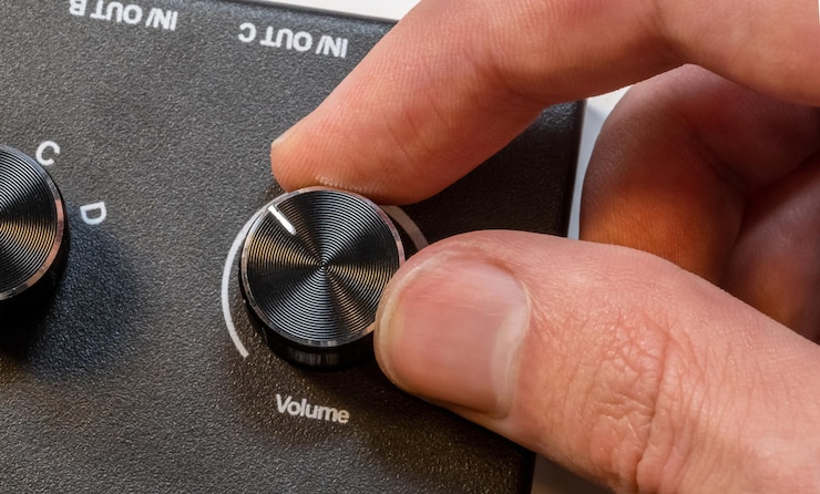 Le dita dell'uomo anonimo sintonizzano finemente una manopola di volume su un elegante pannello di controllo del dispositivo audio regolazione o