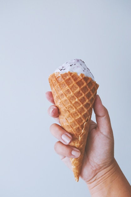 Le dita della mano femminile tengono un cono della cialda con il gelato