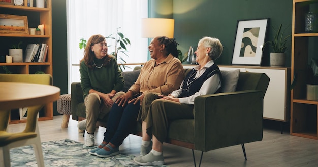 Le donne anziane amici e ridere sul divano con storia divertente ricordo o pettegolezzi con legame in pensione Le persone si rilassano e conversazione con sorriso cura o connessione sul divano in salotto in casa di cura