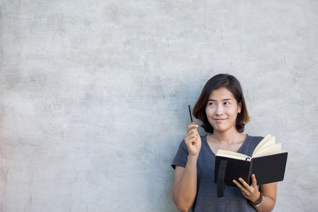 Le donne asiatiche carine stanno pensando qualcosa con il suo libro su sfondo grigio