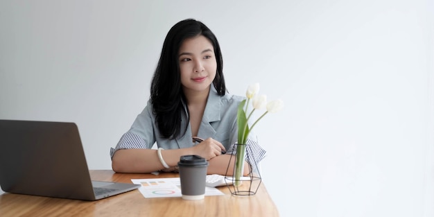 Le donne asiatiche di affari si siedono nell'ufficio e bevono il computer portatile di sguardo del caffè