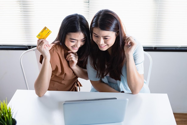 Le donne asiatiche e la sua amica sono entusiaste di usare la tua carta di credito per pagare i tuoi acquisti online e divertirti a fare shopping