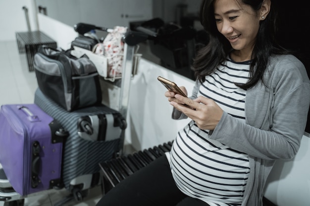 Le donne asiatiche incinte sorridono mentre guardano i loro cellulari