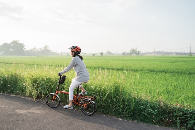 Le donne asiatiche indossano caschi per andare in bici pieghevole nelle risaie