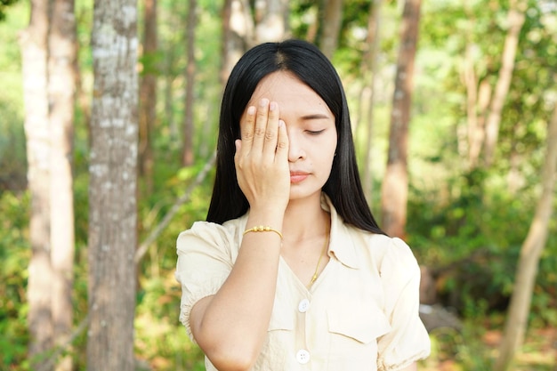 Le donne asiatiche si coprono gli occhi con entrambe le mani sullo sfondo della natura