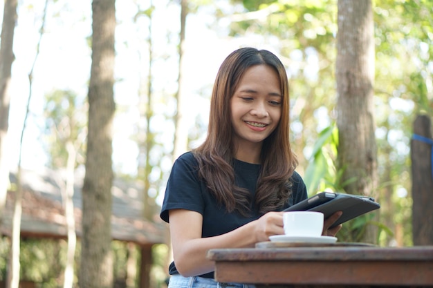 Le donne asiatiche sono felici di sedersi e lavorare in un bar Ci sono alberi verdi circondati dalla natura