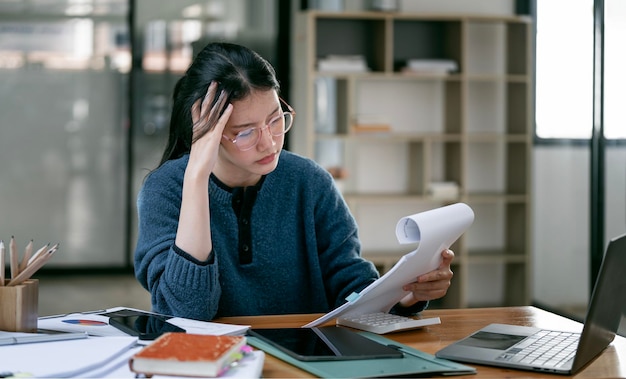 Le donne asiatiche sono stressate mentre lavorano al documento in mano Donna d'affari asiatica stanca con mal di testa in ufficio che si sente male al lavoro