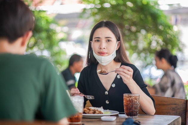 Le donne asiatiche usano la maschera che si siede nel fuoco molle del ristorante, nuovo concetto normale