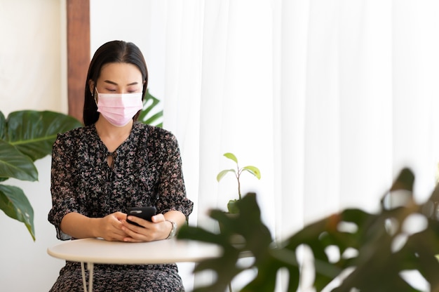 Le donne che lavorano indossano la maschera per il viso tenendo lo smartphone seduti a casa lavorando
