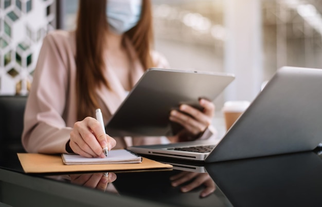 Le donne d'affari lavorano a mano su un tablet e scrivono su un blocco note con una penna in ufficio