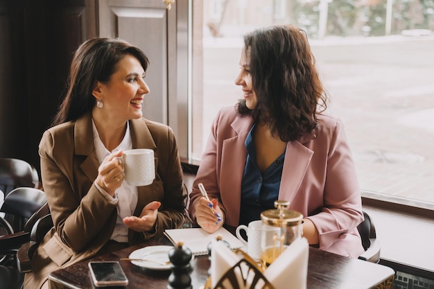 Le donne d'affari si siedono in un bar, bevono caffè e hanno una conversazione d'affari, discutono di affari e si divertono