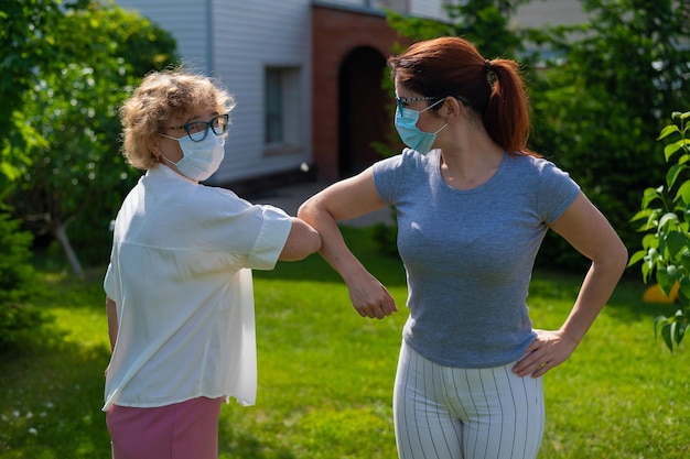 Le donne in maschera medica salutano i gomiti fuori Una donna anziana e sua figlia adulta mantengono una distanza sociale nel parco durante l'epidemia di coronavirus Nuova stretta di mano che urta i gomiti