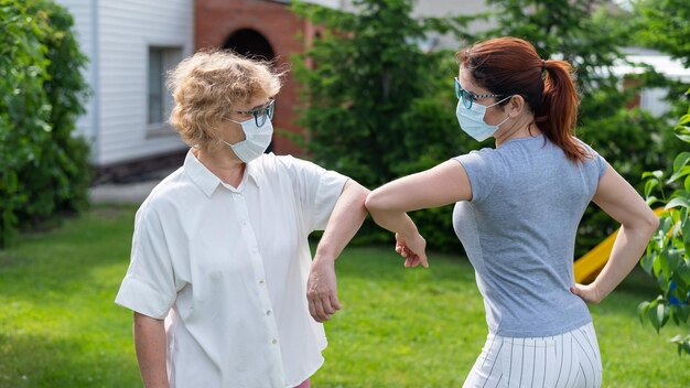 Le donne in maschera medica salutano i gomiti fuori Una donna anziana e sua figlia adulta mantengono una distanza sociale nel parco durante l'epidemia di coronavirus Nuova stretta di mano che urta i gomiti