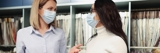 Le donne in maschere mediche protettive sfogliano il catalogo dei campioni di tessuto in negozio durante il lavoro